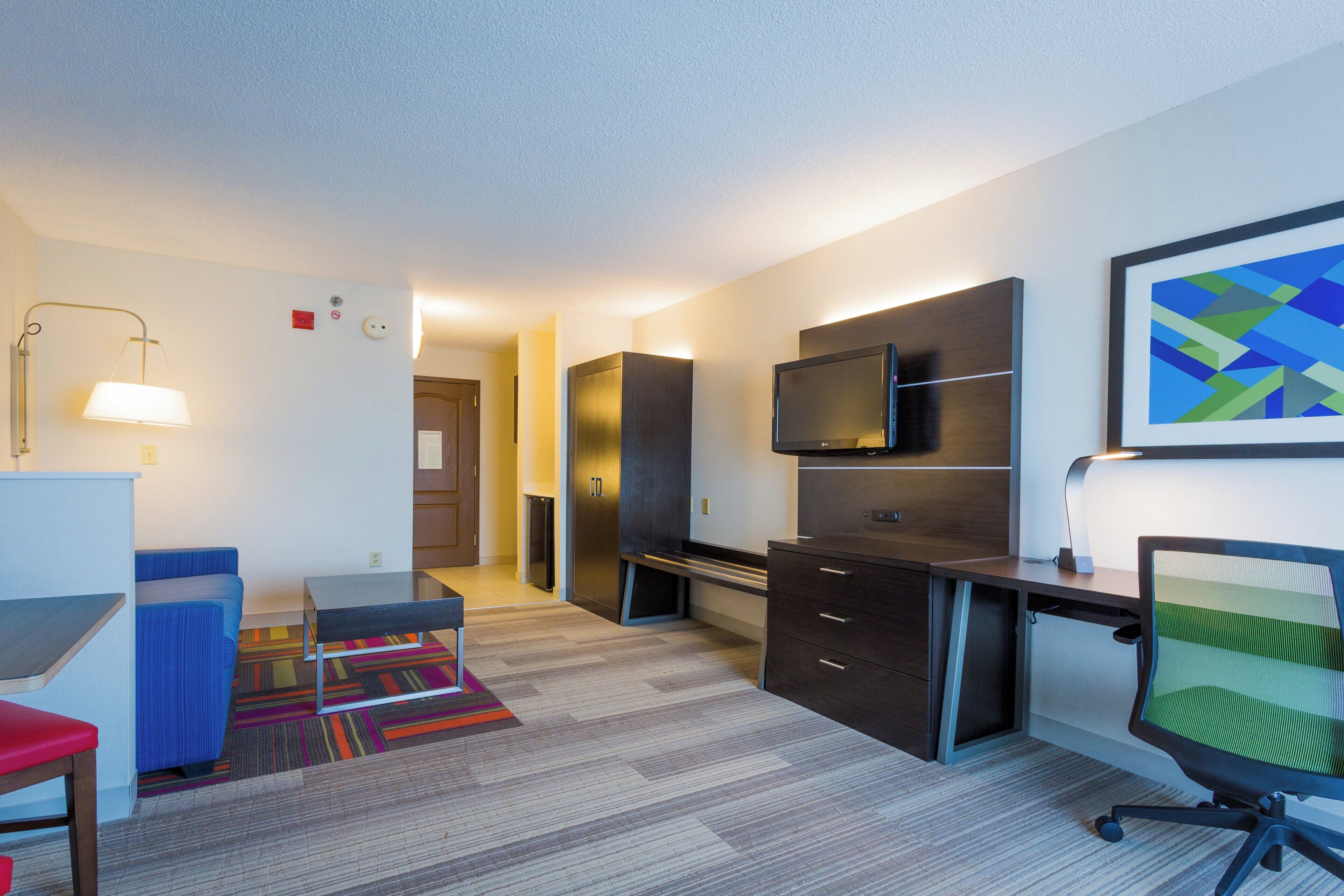 Una habitación de hotel moderna con escritorio, silla, televisión y una alfombra colorida.