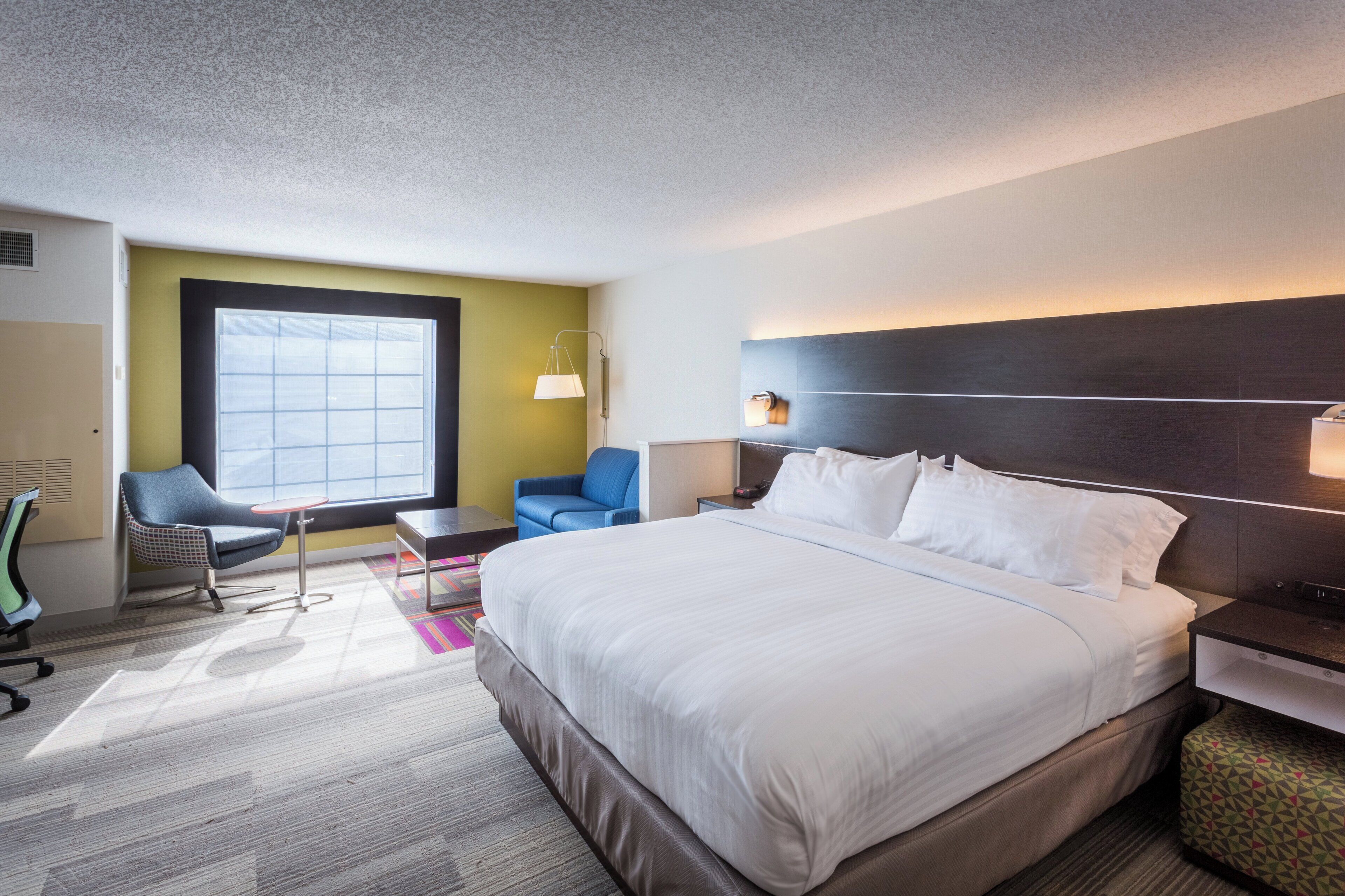 A hotel room with a large bed, a desk, a chair, and a window.