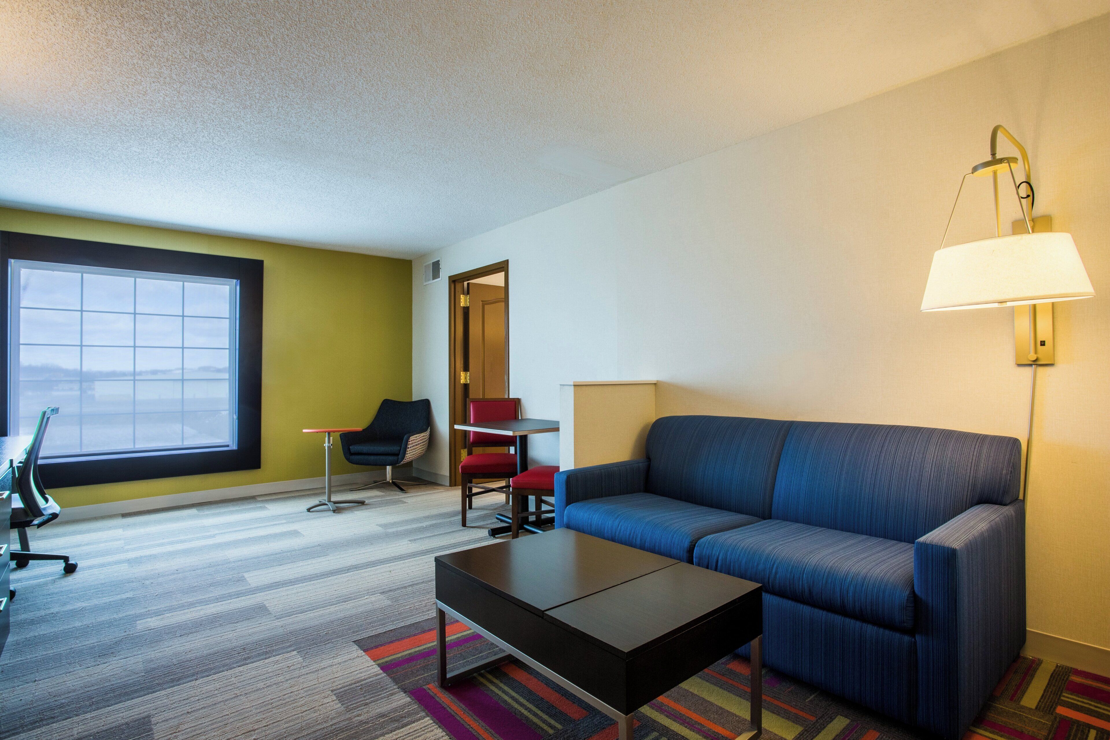 Een hotelkamer met een bank, een tafeltje, een stoel, een lamp en een raam.