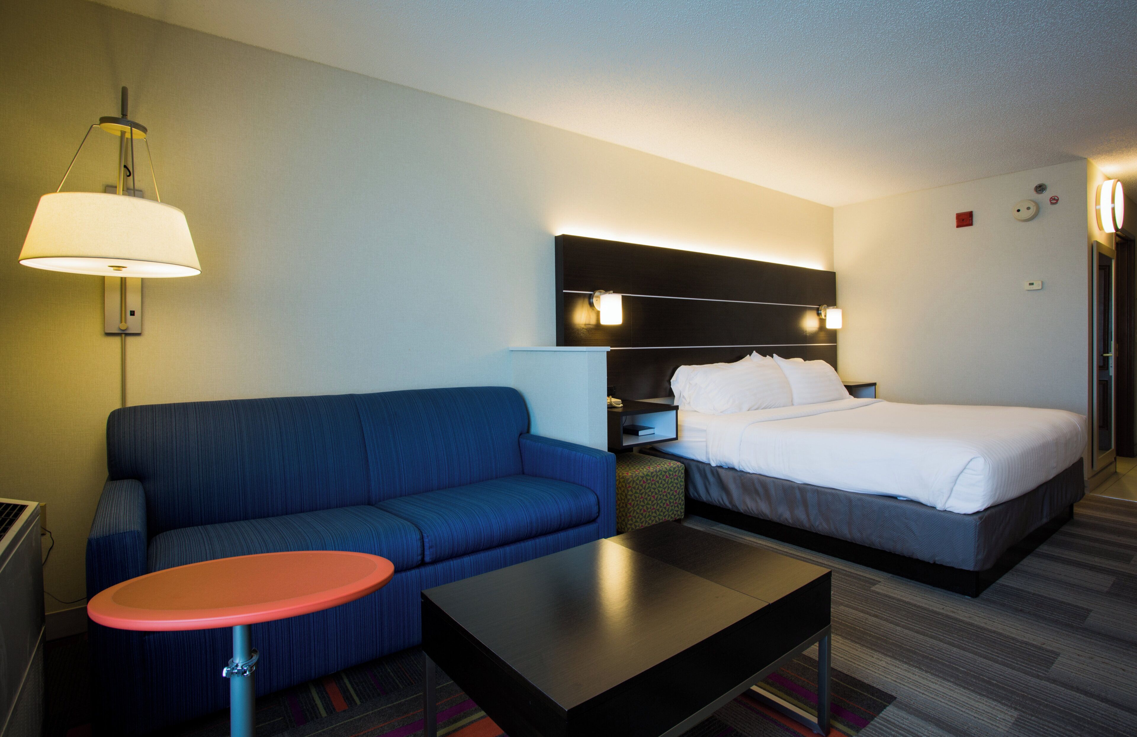 A hotel room with a bed, a sofa, a small table, and a lamp.
