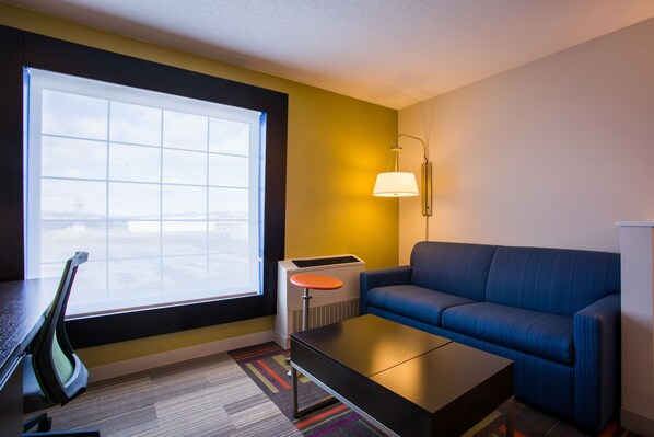 A modern hotel room with a large window, a blue sofa, a small round table, and a desk with a chair. - Holiday Inn Express & Suites Reading by IHG (Reading)
