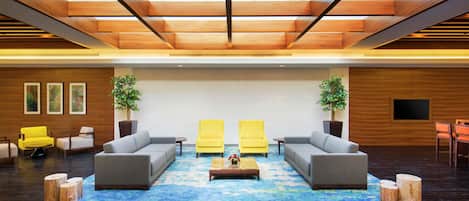 Een ruime lobby met een modern design, met een grote zithoek met banken en fauteuils, een bijzettafeltje en twee potplanten.