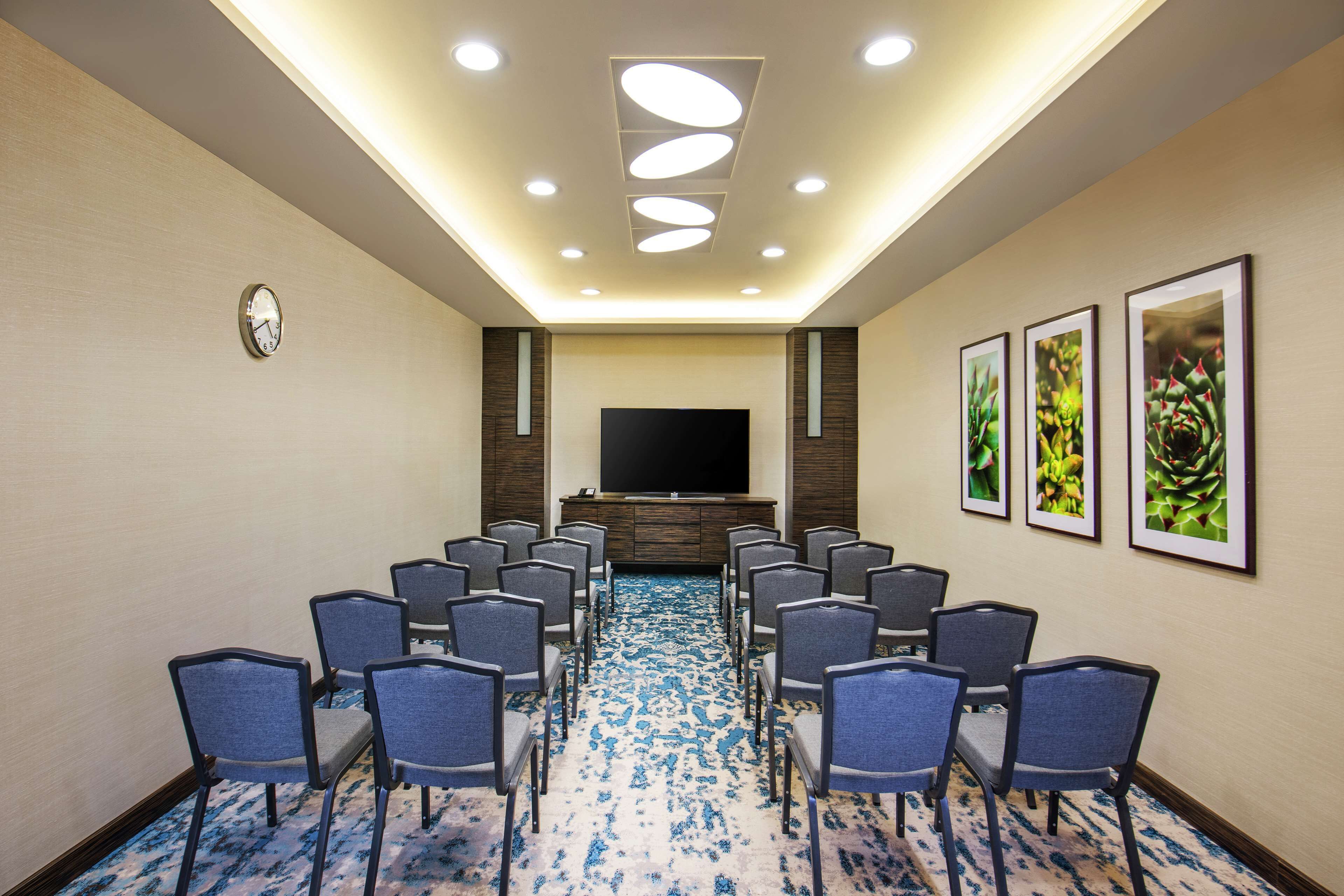 A conference room with a flat-screen TV, rows of chairs, a clock, and framed pictures on the walls.
