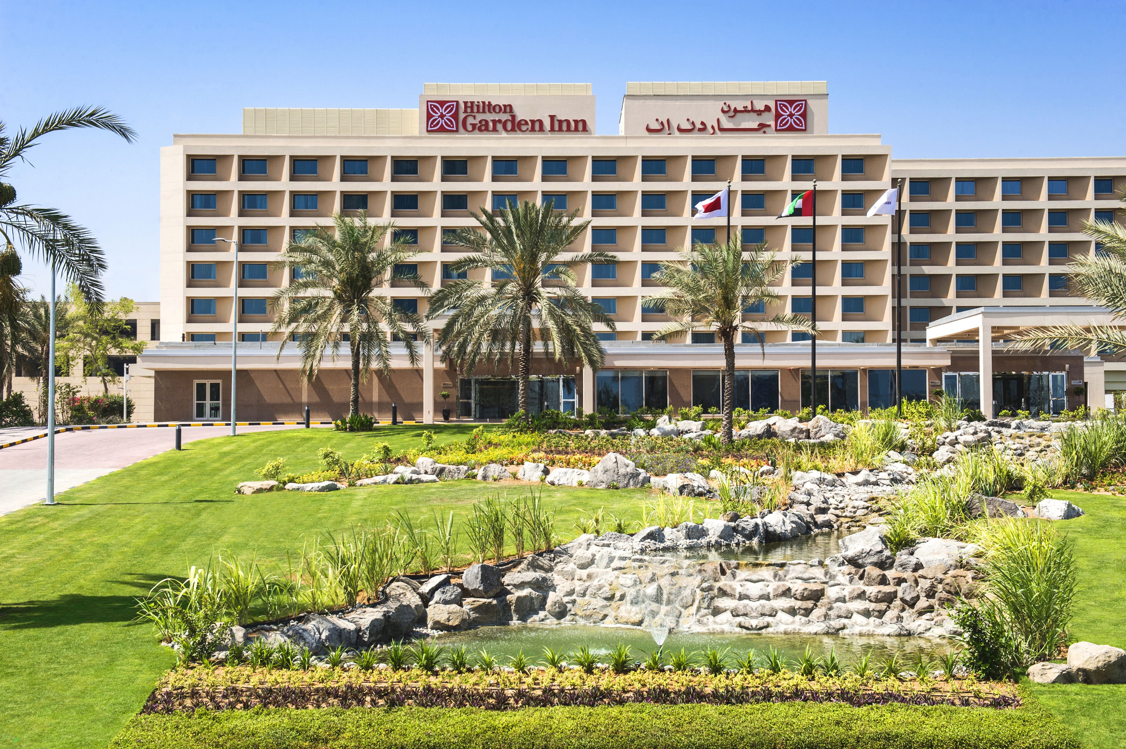 Un hotel Hilton Garden Inn con un giardino curato, palme e una piccola cascata.