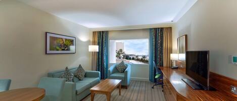 A hotel room with a sofa, a coffee table, a TV, and a window with curtains.