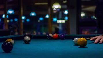 A pool table with balls in various colors, a pool cue, and a person's hand reaching for a ball.