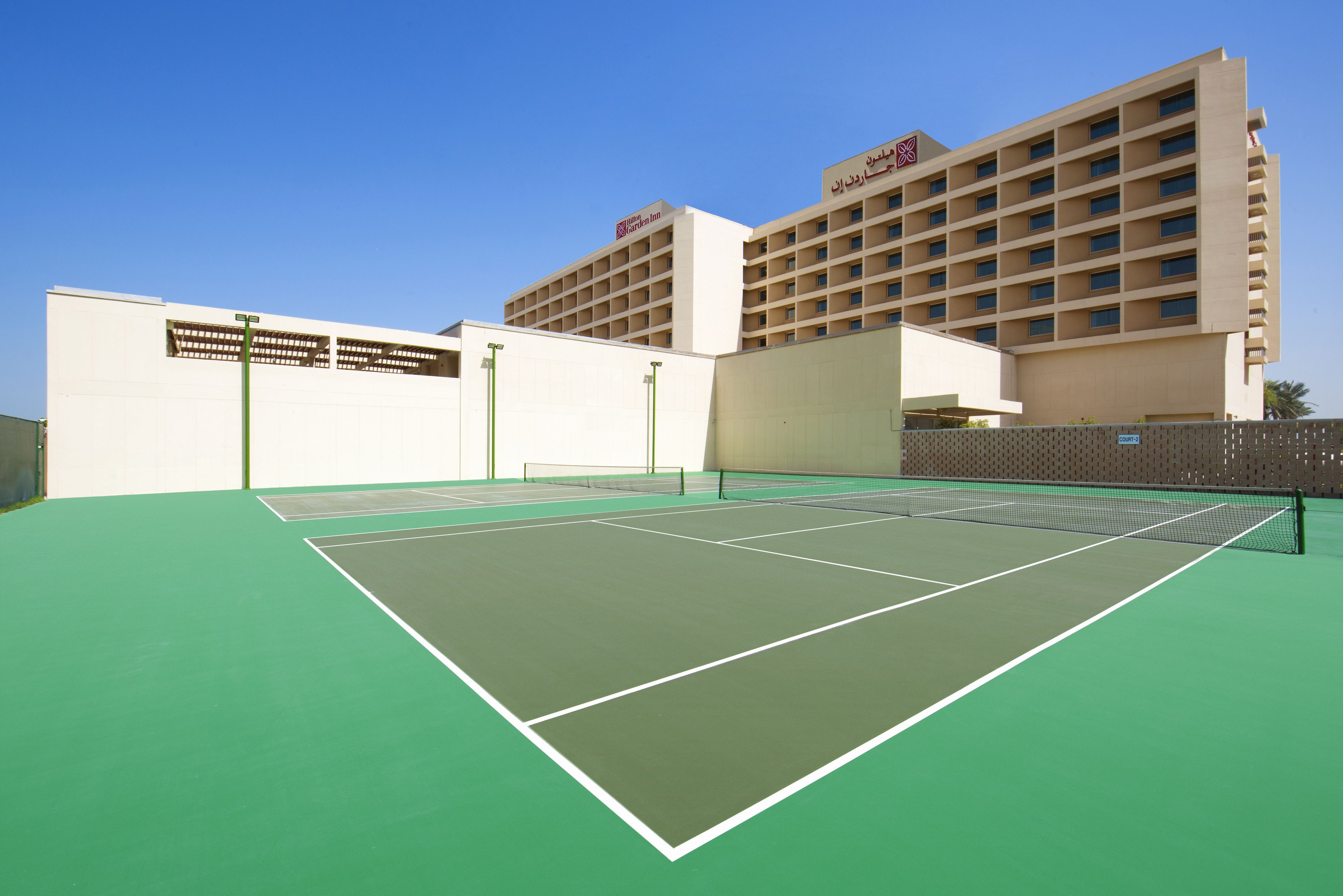 Ein Hallen-Tennisplatz mit grüner Oberfläche, umgeben von einem weißen Gebäude mit zahlreichen Fenstern und einem Schild, das ein Marriott Hotel kennzeichnet.