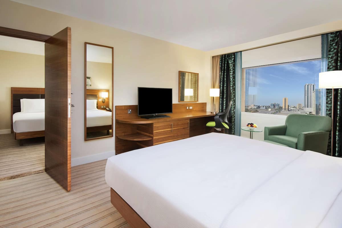 A hotel room with a large bed, a desk with a TV, a chair, and a view of the city.
