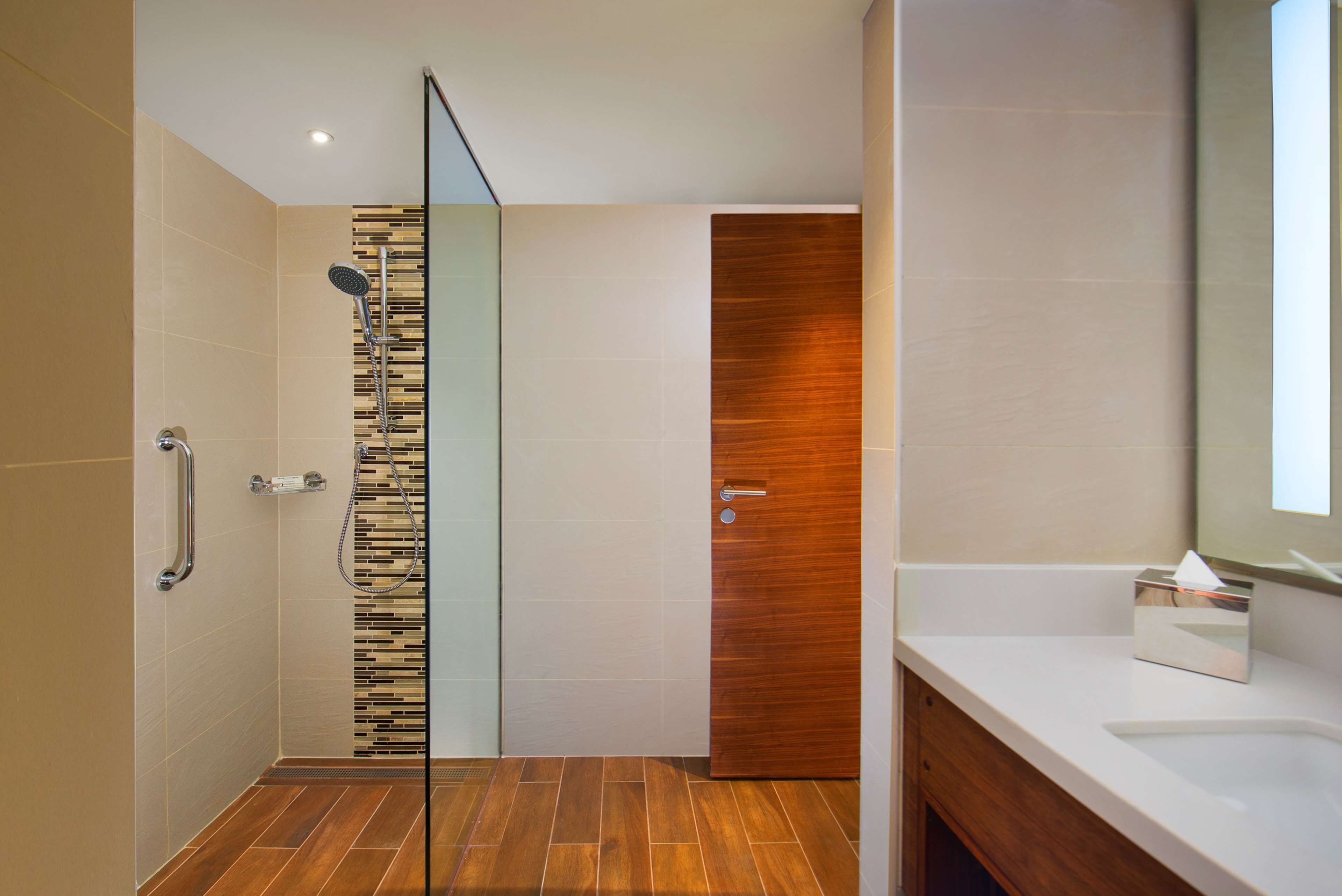 Un baño moderno con ducha, pared de paneles de madera y lavamanos blanco.