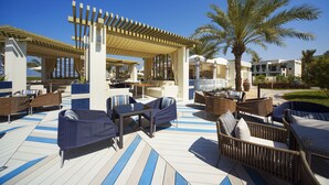 An outdoor lounge area with wicker furniture, a pergola, and palm trees.