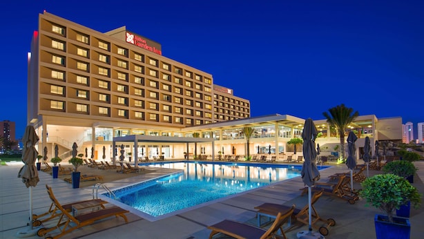 A hotel with a swimming pool, sun loungers, and umbrellas.