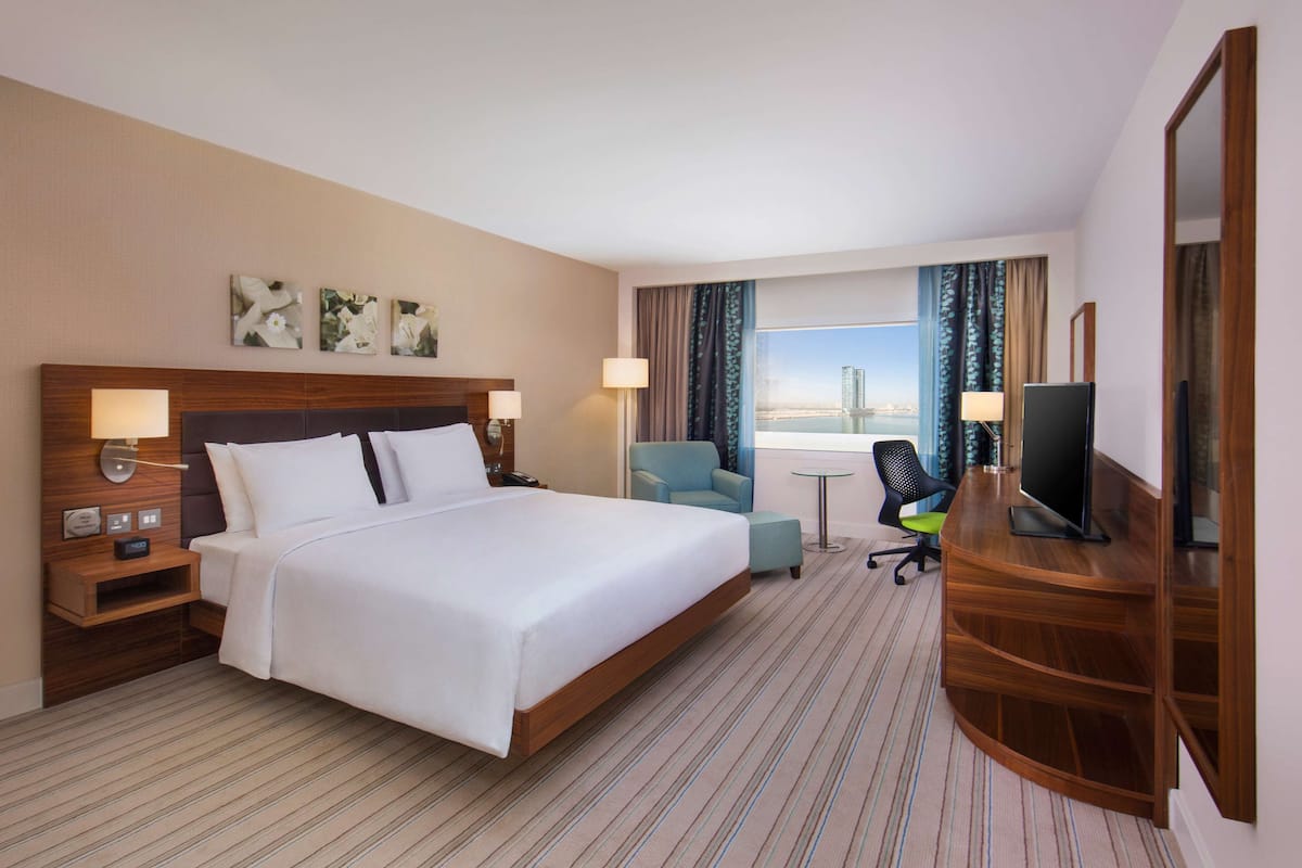 A hotel room with a large bed, a desk with a TV, a chair, and a view of the cityscape.