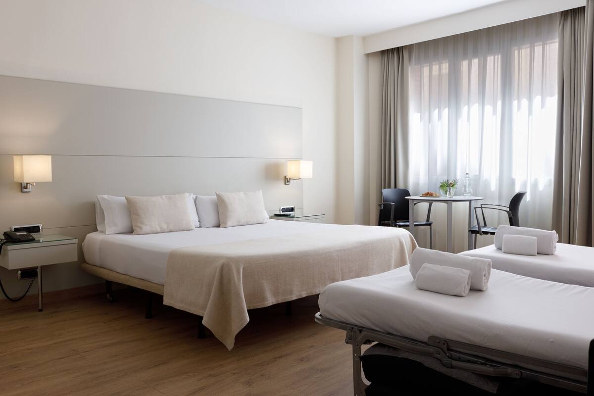 Une chambre d’hôtel avec un grand lit, deux tables de chevet, un bureau avec une chaise et une fenêtre avec des rideaux.