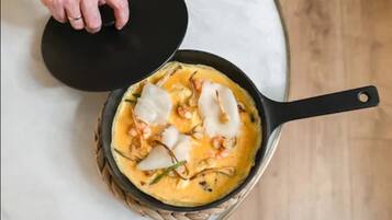 Una persona levantando la tapa de una sartén con un plato de mariscos y vegetales.