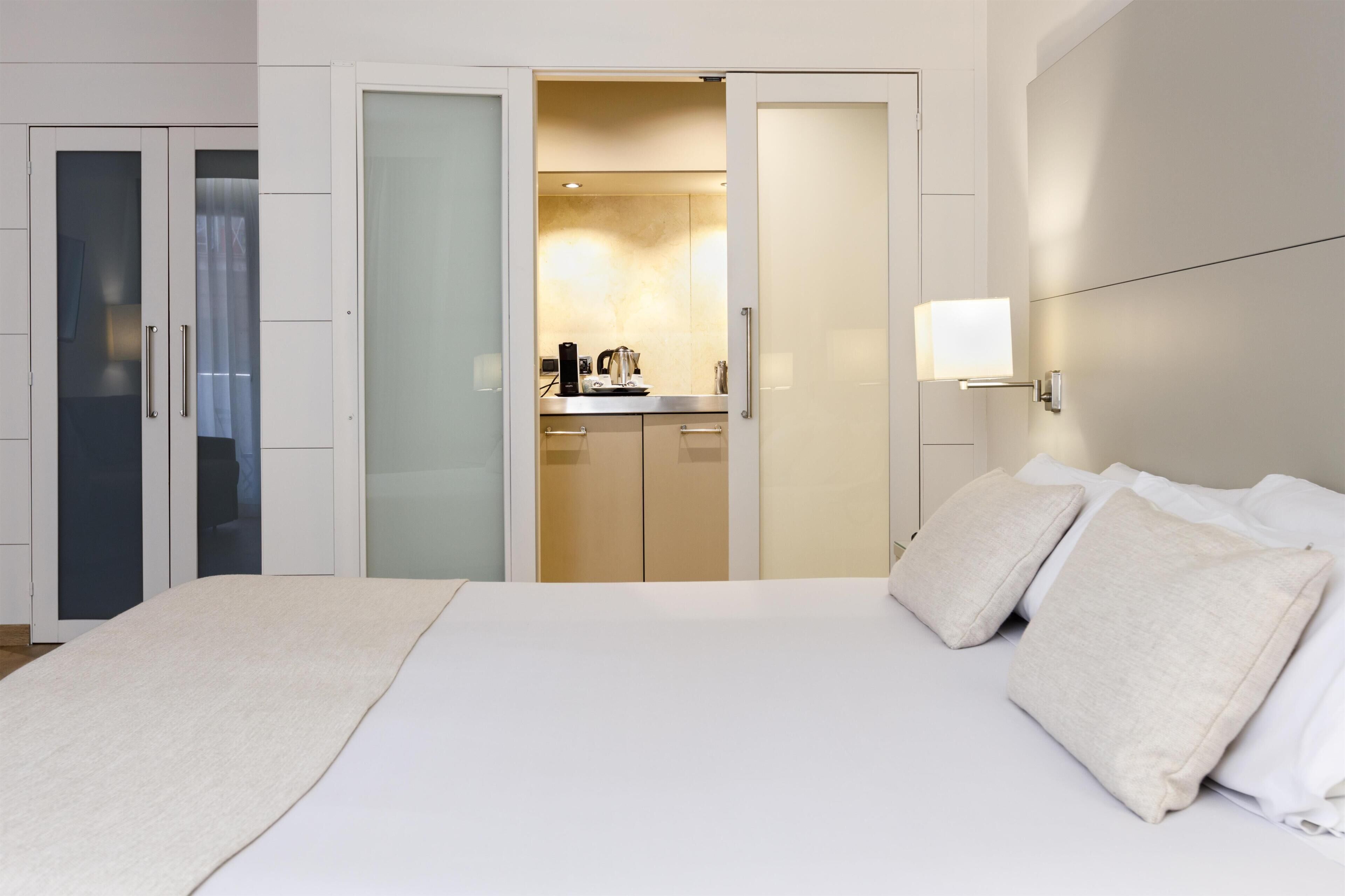 A hotel room with a bed, a bedside table, a nightstand, a wardrobe, and a bathroom visible through an open door.
