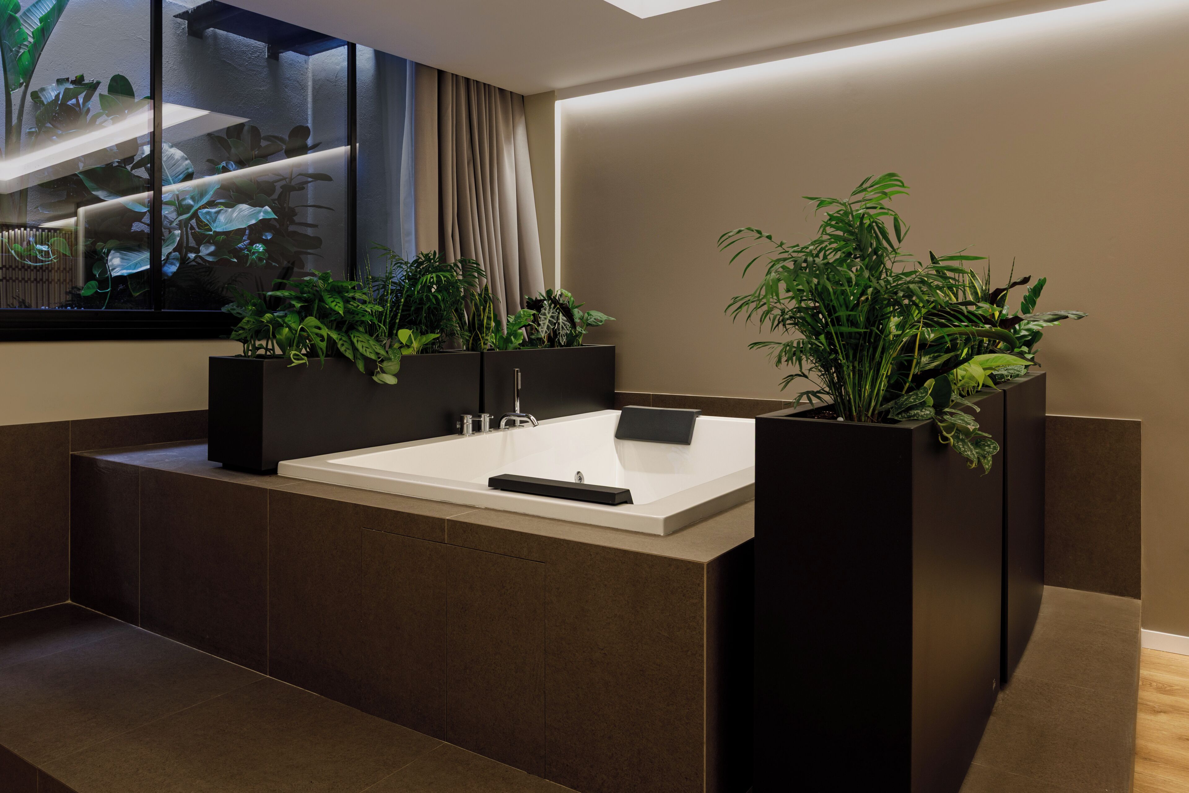 Un baño moderno con una bañera grande, muebles oscuros y plantas en macetas.