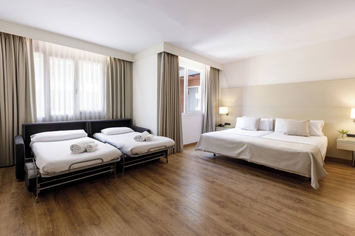 Une chambre d’hôtel avec deux lits, un plancher en bois, une fenêtre avec des rideaux et une table de chevet avec une lampe.