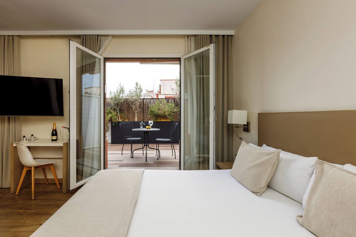 Une chambre d’hôtel comprenant un lit, un bureau, une chaise, une télévision et un balcon avec une table et des chaises.
