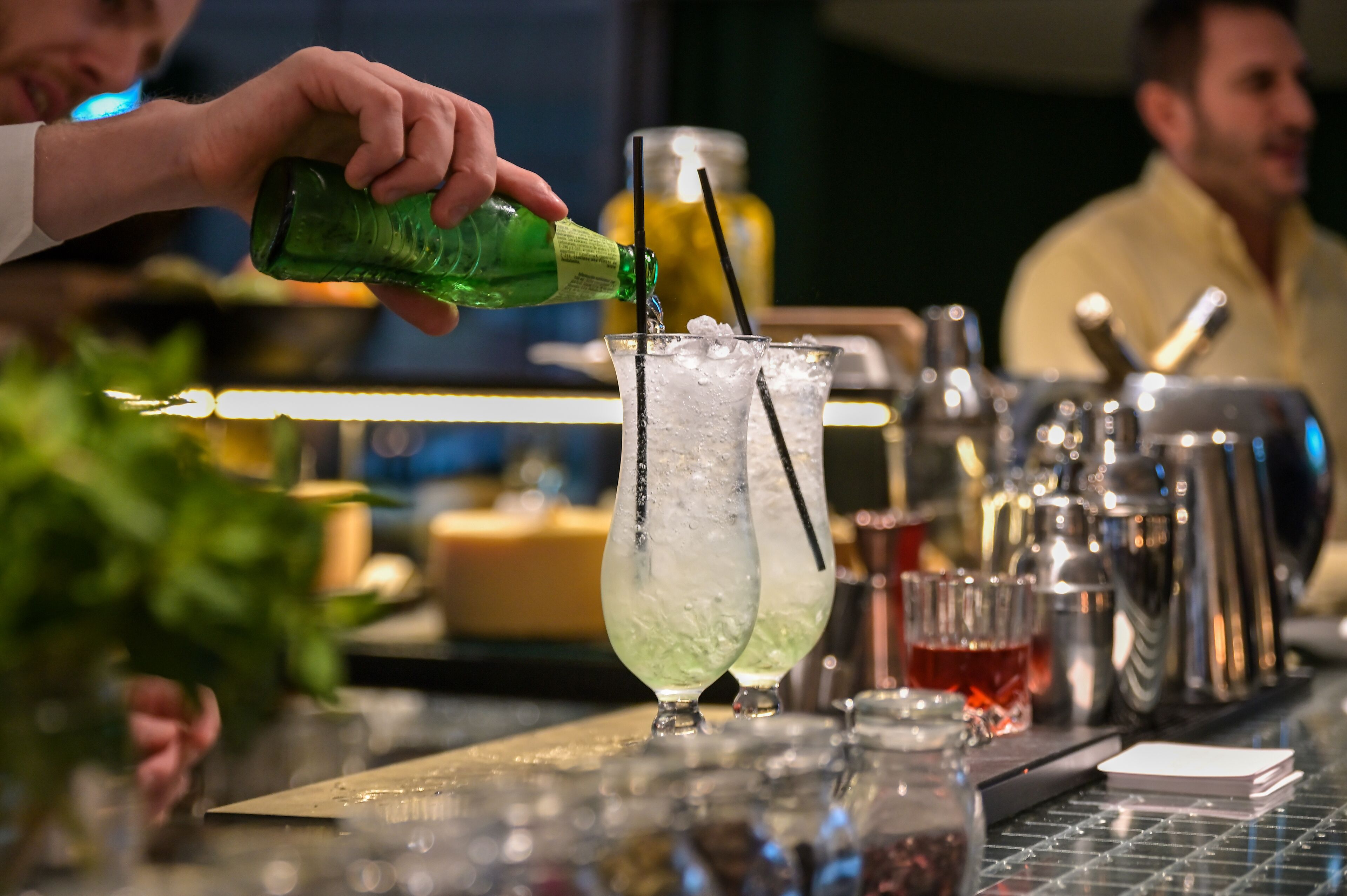 Een bartender schenkt een drankje in een glas met ijs en een rietje.