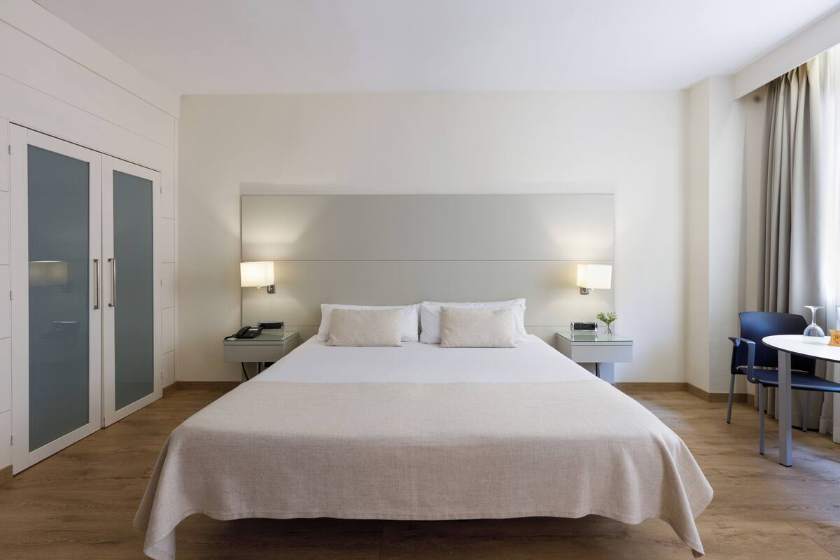 Une chambre d’hôtel avec un grand lit, des tables de chevet, un bureau avec une chaise et une armoire.