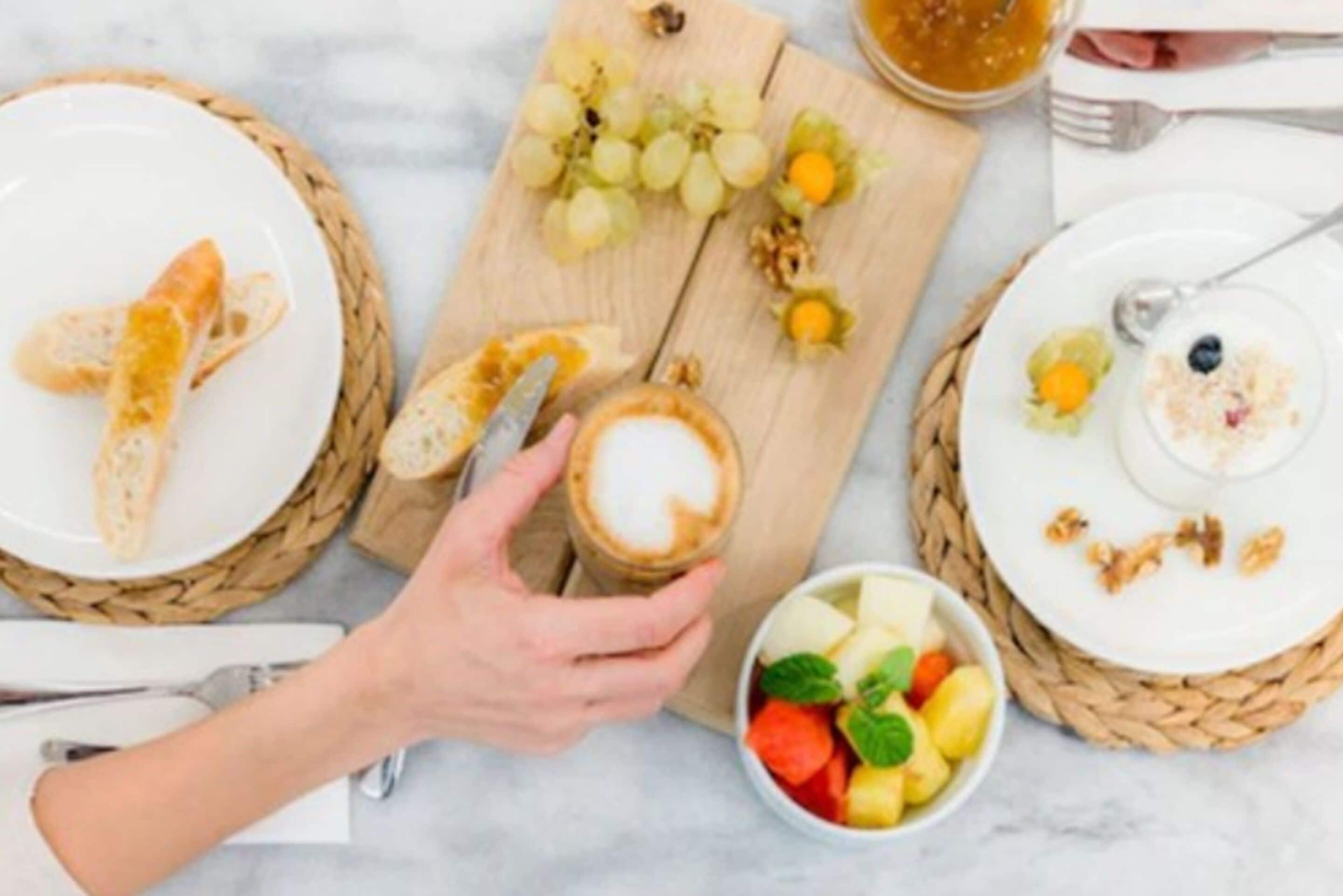 A breakfast setting with croissants, a cup of coffee, a bowl of fruit, and a plate with yogurt and granola.