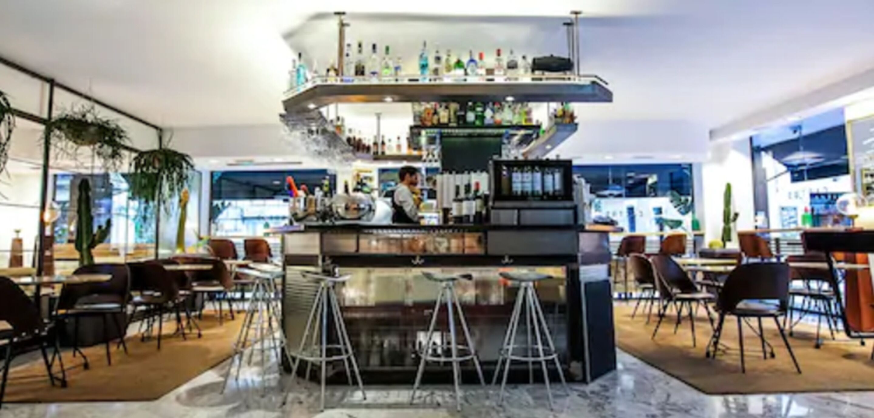 Zona de bar moderna con una barra central, distintas opciones de asientos y una variedad de botellas en estantes.