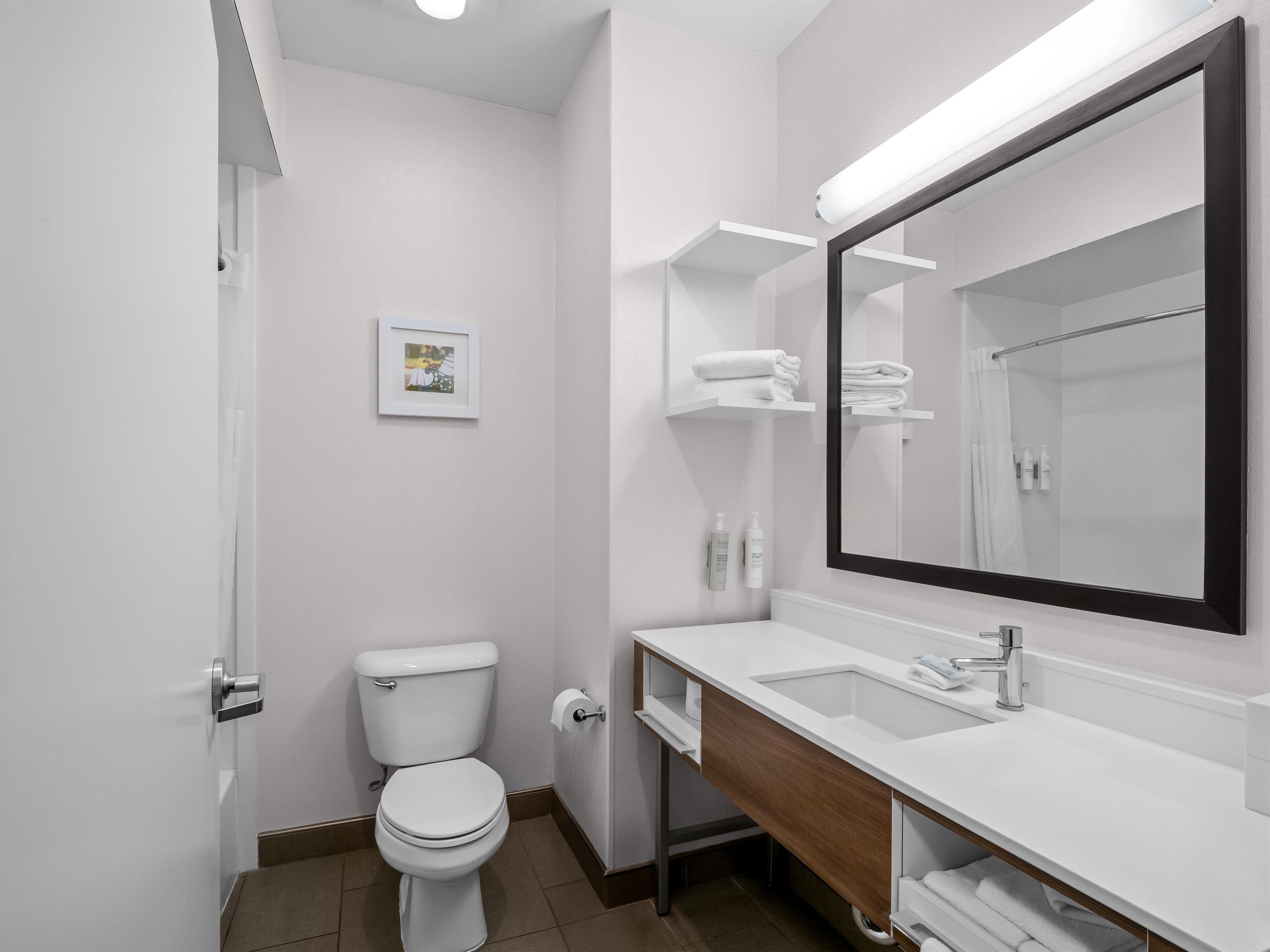 A modern bathroom with a toilet, sink, mirror, and towel racks.