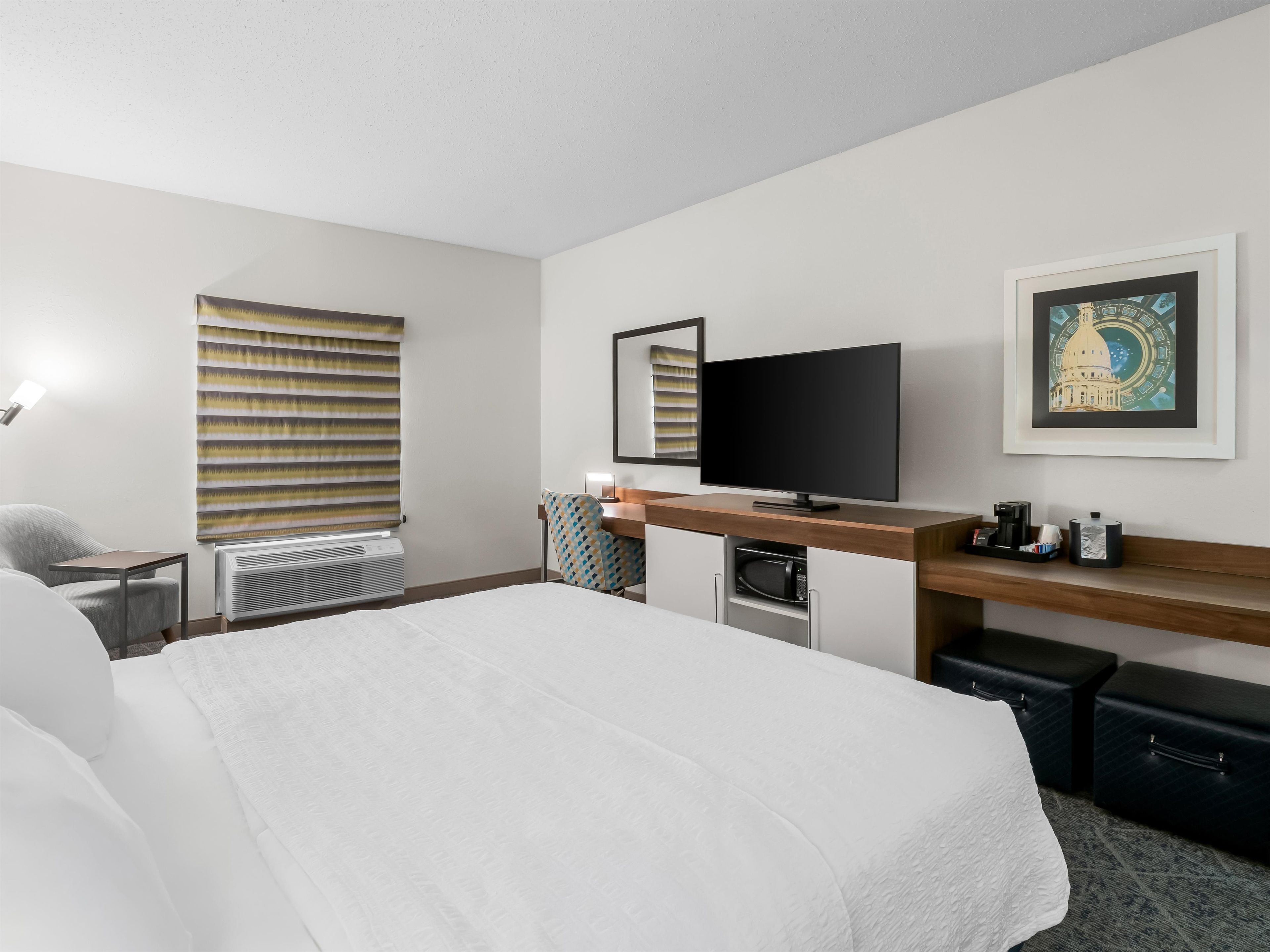 A hotel room with a bed, a television, a desk, a chair, a microwave, and a framed picture on the wall.