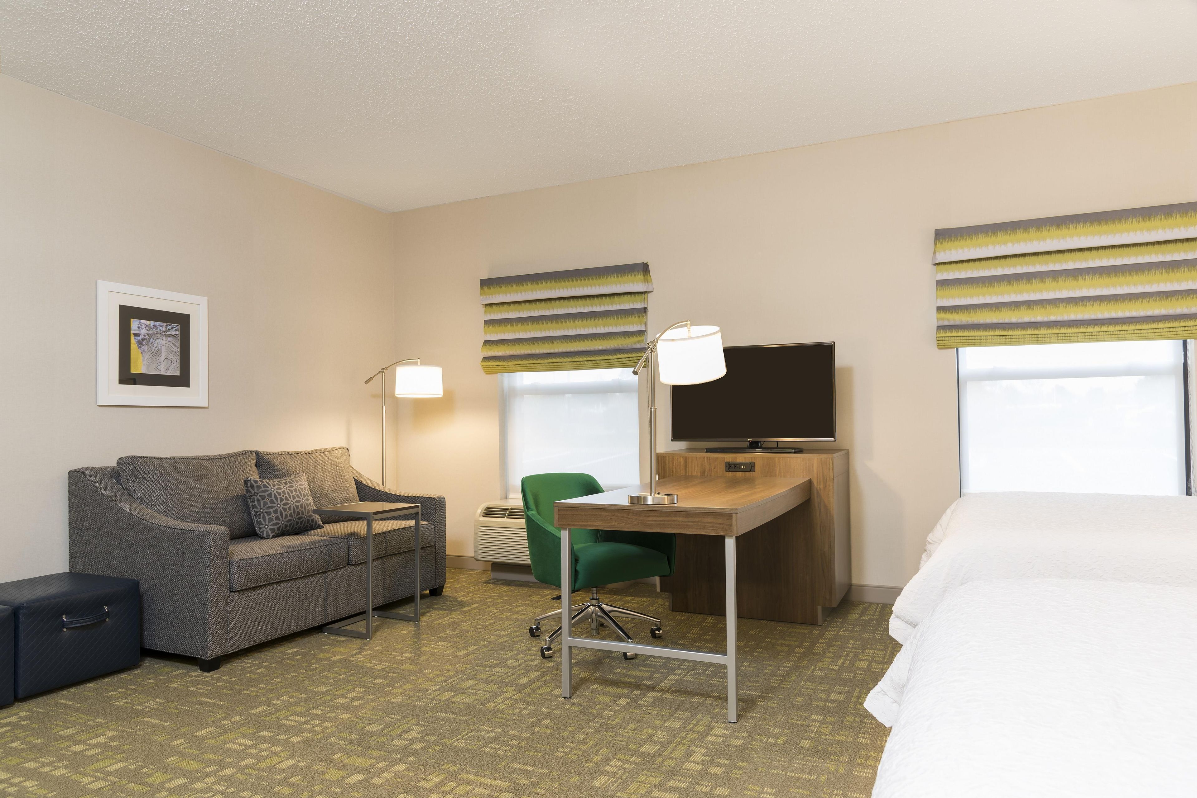 A hotel room with a sofa, a desk, a television, and a bed.