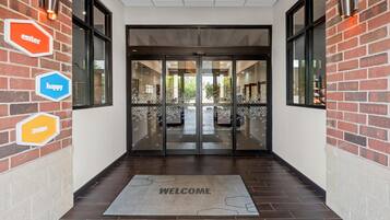 A modern entrance with a welcome mat, glass doors, and brick walls.
