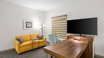 Una habitación moderna con un sofá amarillo, un escritorio de madera, un televisor de pantalla plana grande y una pared con diseño.