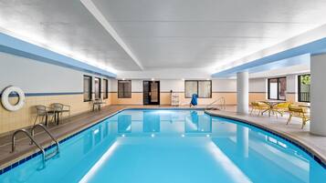 An indoor swimming pool with clear water, surrounded by seating areas and a lifebuoy on the wall.
