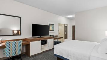 A hotel room with a bed, a desk with a chair, a television, a wardrobe, and a mirror.