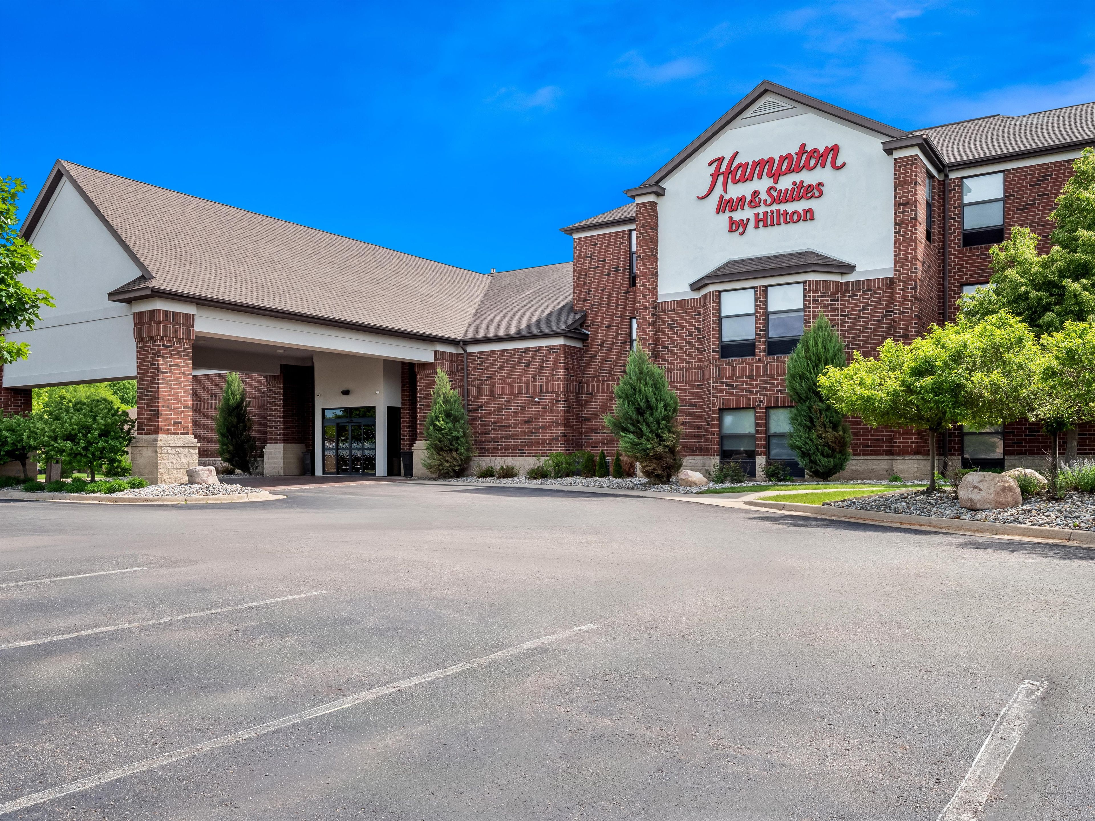 A Hampton Inn & Suites by Hilton with a brick facade, a covered entrance, and a parking lot.