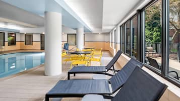 A poolside area with lounge chairs, a pool, and large windows offering a view of the outdoors.