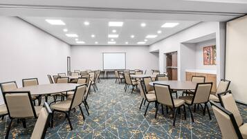 A conference room with multiple tables and chairs, a projector screen, and a patterned carpet.