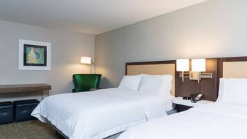 A hotel room with two beds, a desk, a chair, and a wall-mounted lamp.