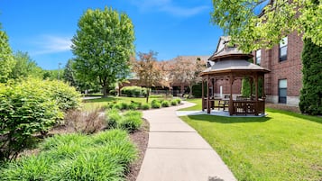 A gazebo in a well-maintained garden with a brick building in the background.