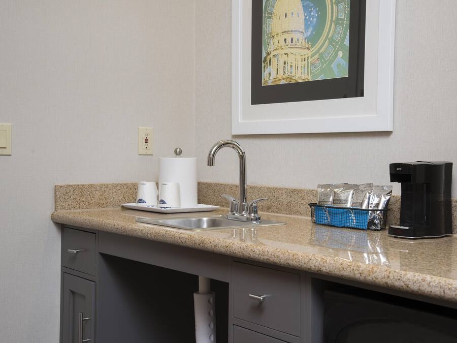 A kitchen with a granite countertop, a stainless steel sink, a coffee maker, and a framed picture on the wall.