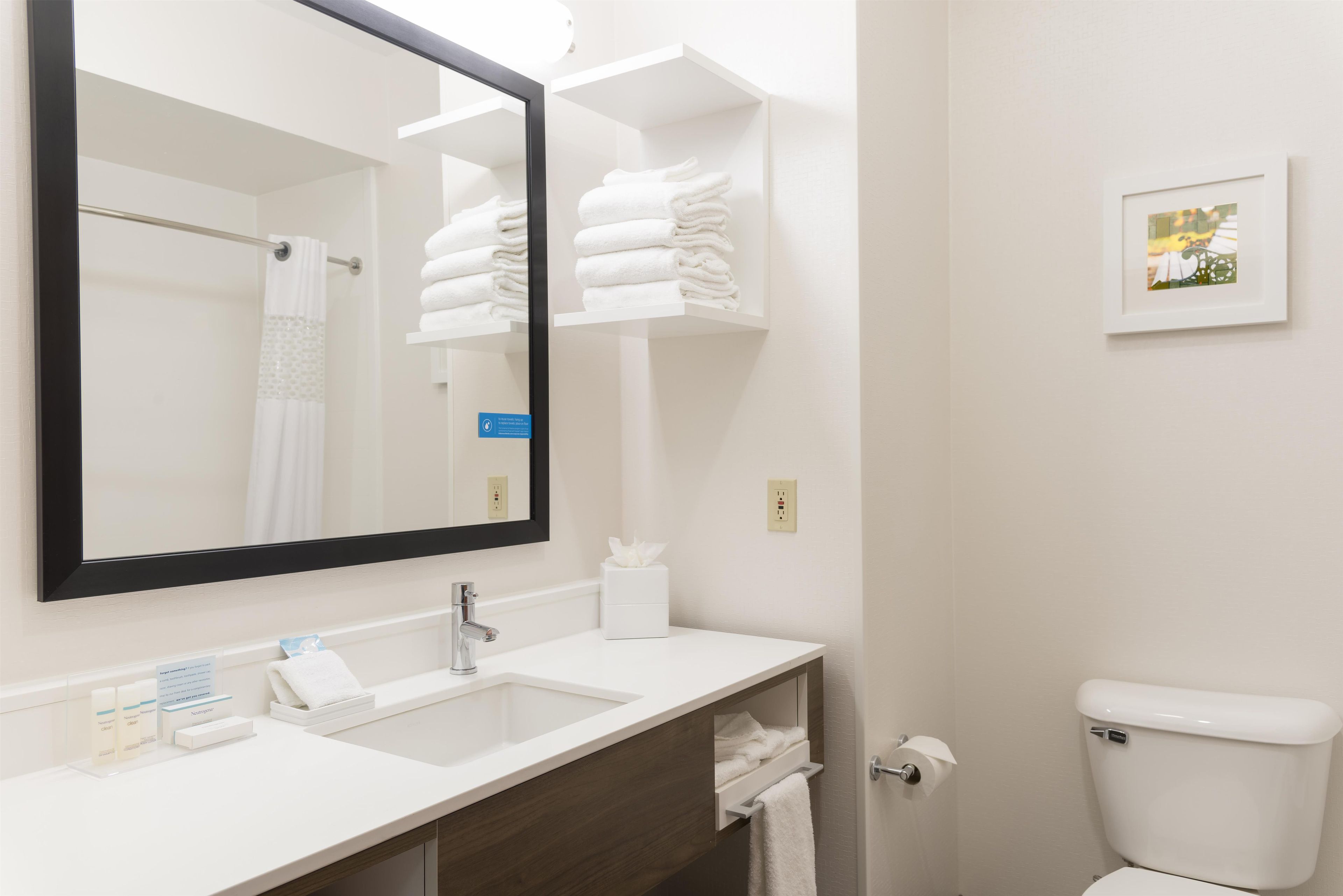 Une salle de bain avec un lavabo blanc, un miroir, un porte-serviettes, des toilettes et un petit tableau encadré accroché au mur.