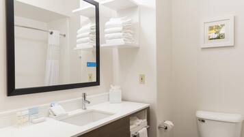 Une salle de bain avec un lavabo blanc, un miroir, un porte-serviettes, des toilettes et un petit tableau encadré accroché au mur.