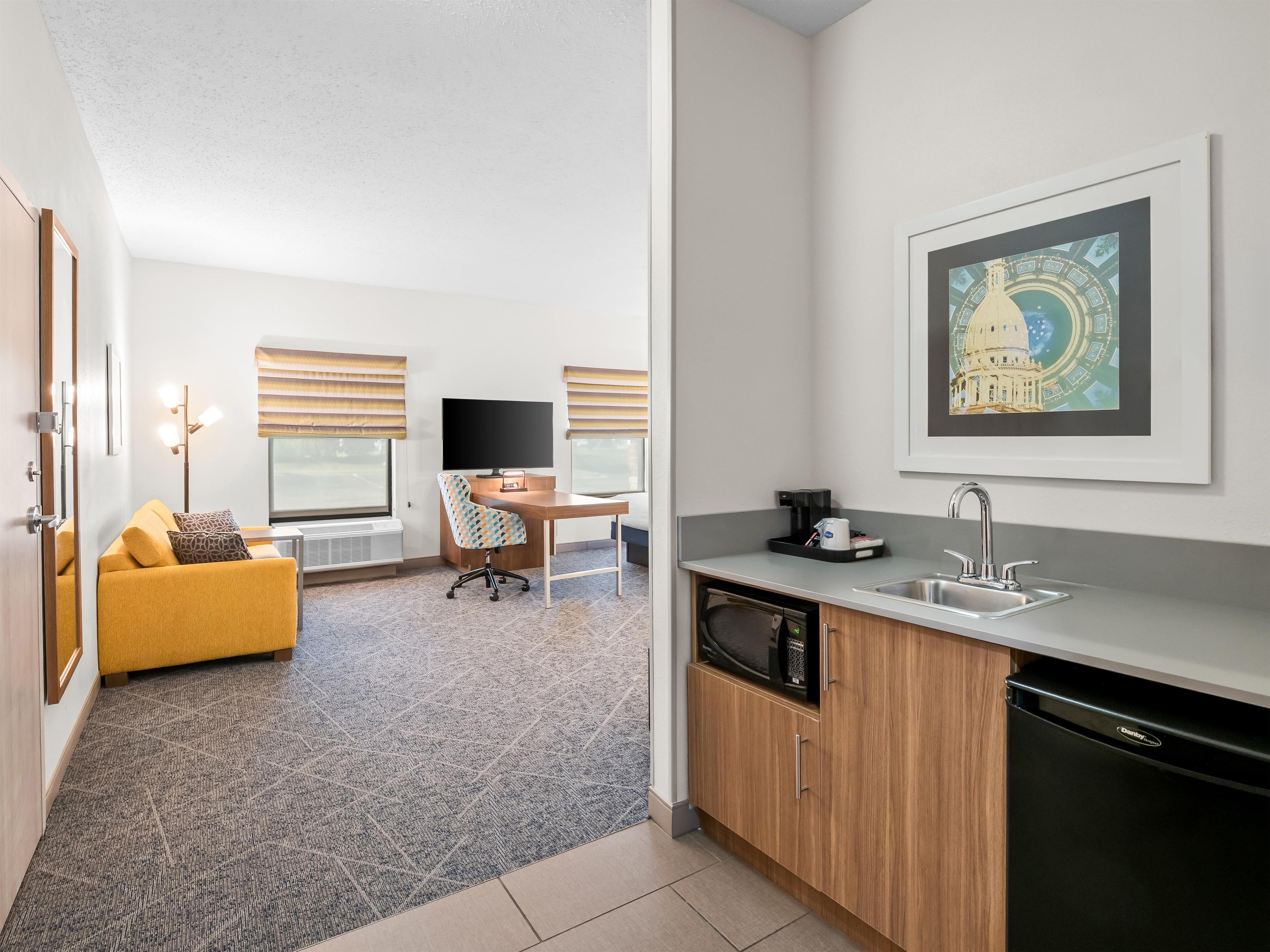 A modern hotel room with a sofa, desk, and kitchenette.