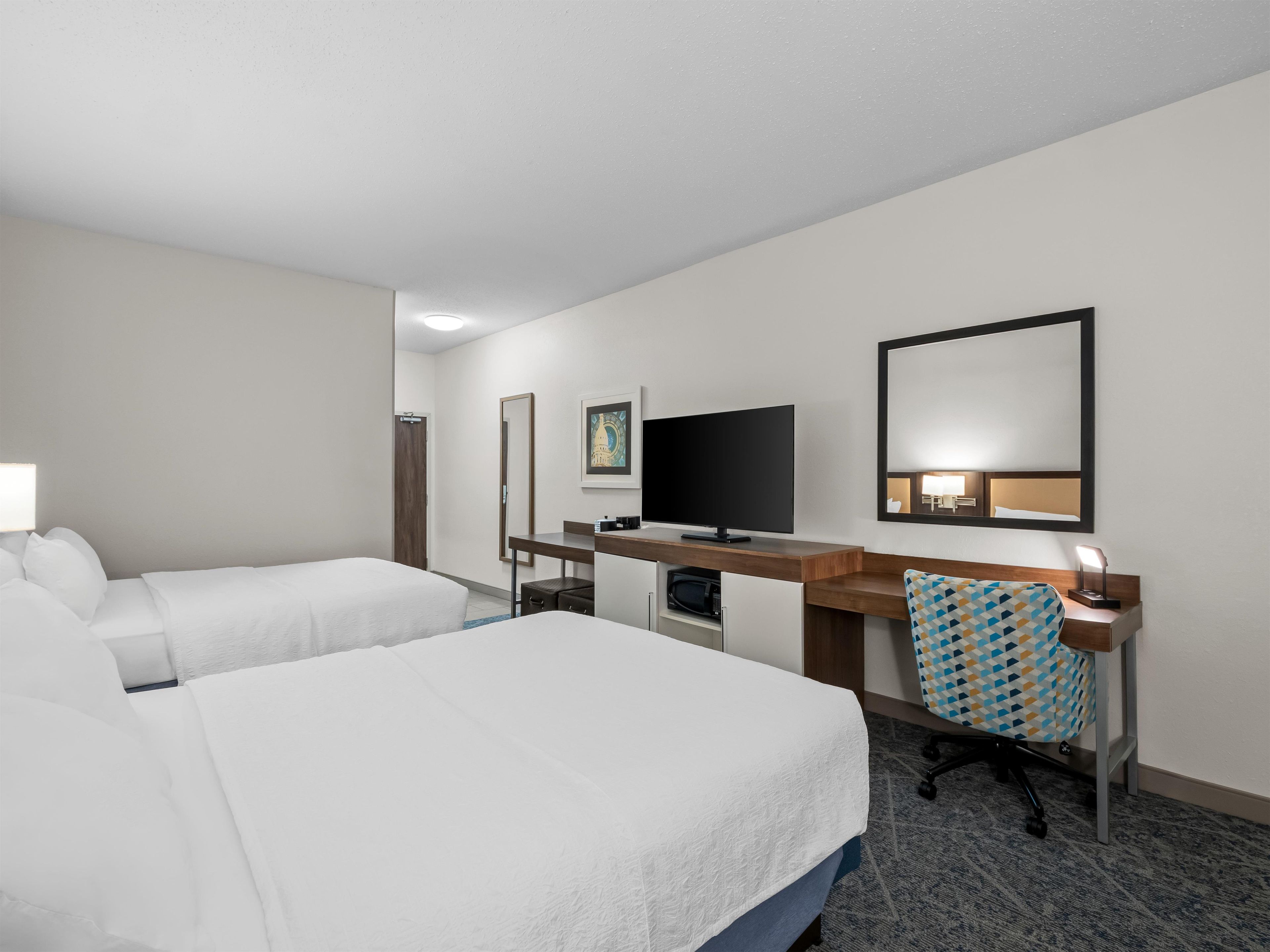 A hotel room with two beds, a desk with a TV, a mirror, and a chair.