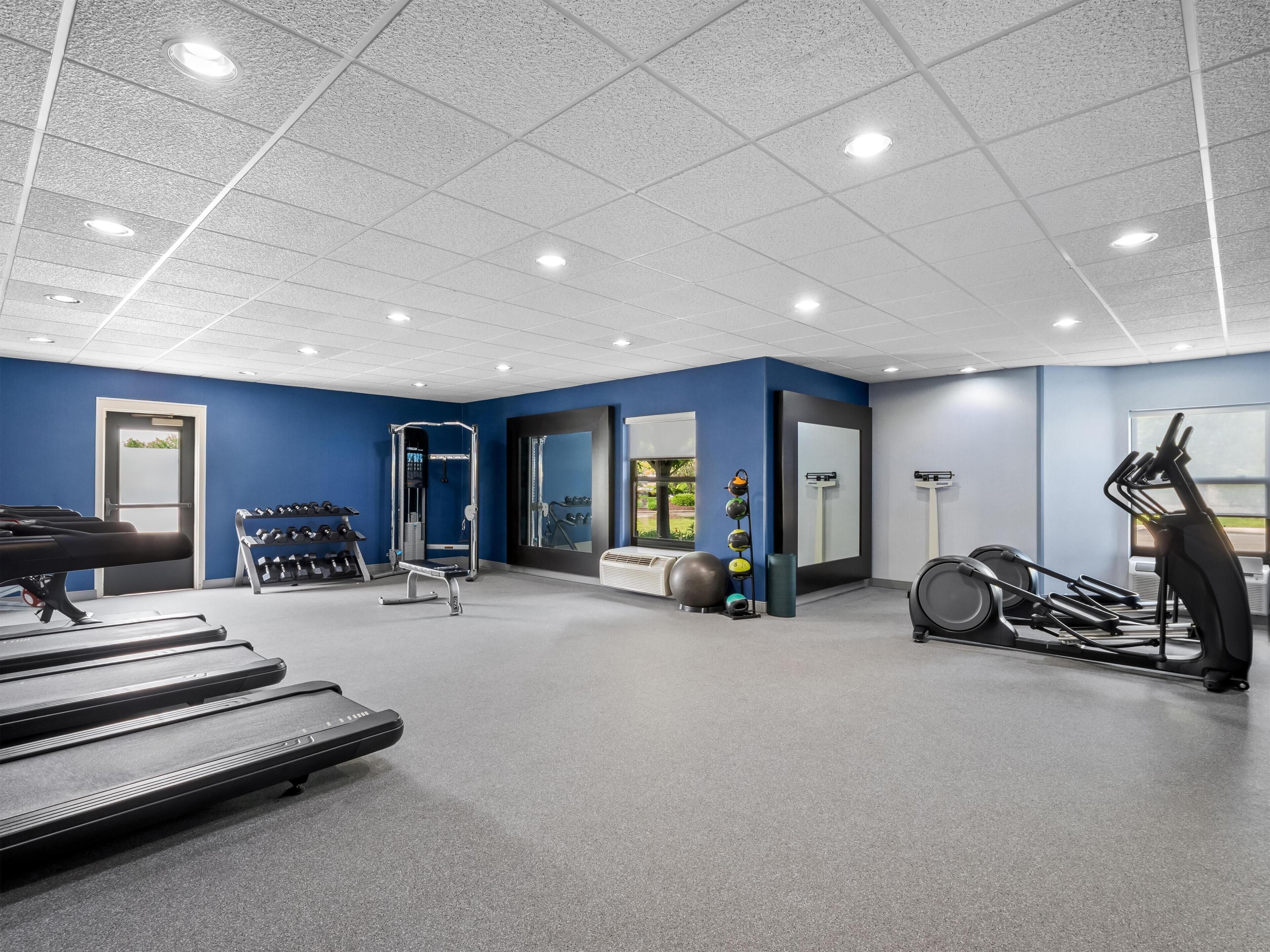Une salle de sport équipée de tapis de course, d’une machine de musculation et de ballons d’exercice.
