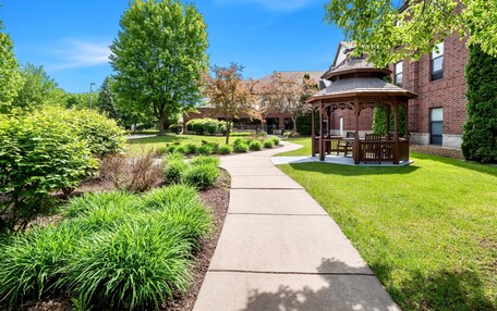 A gazebo in a well-maintained garden with a brick building in the background.