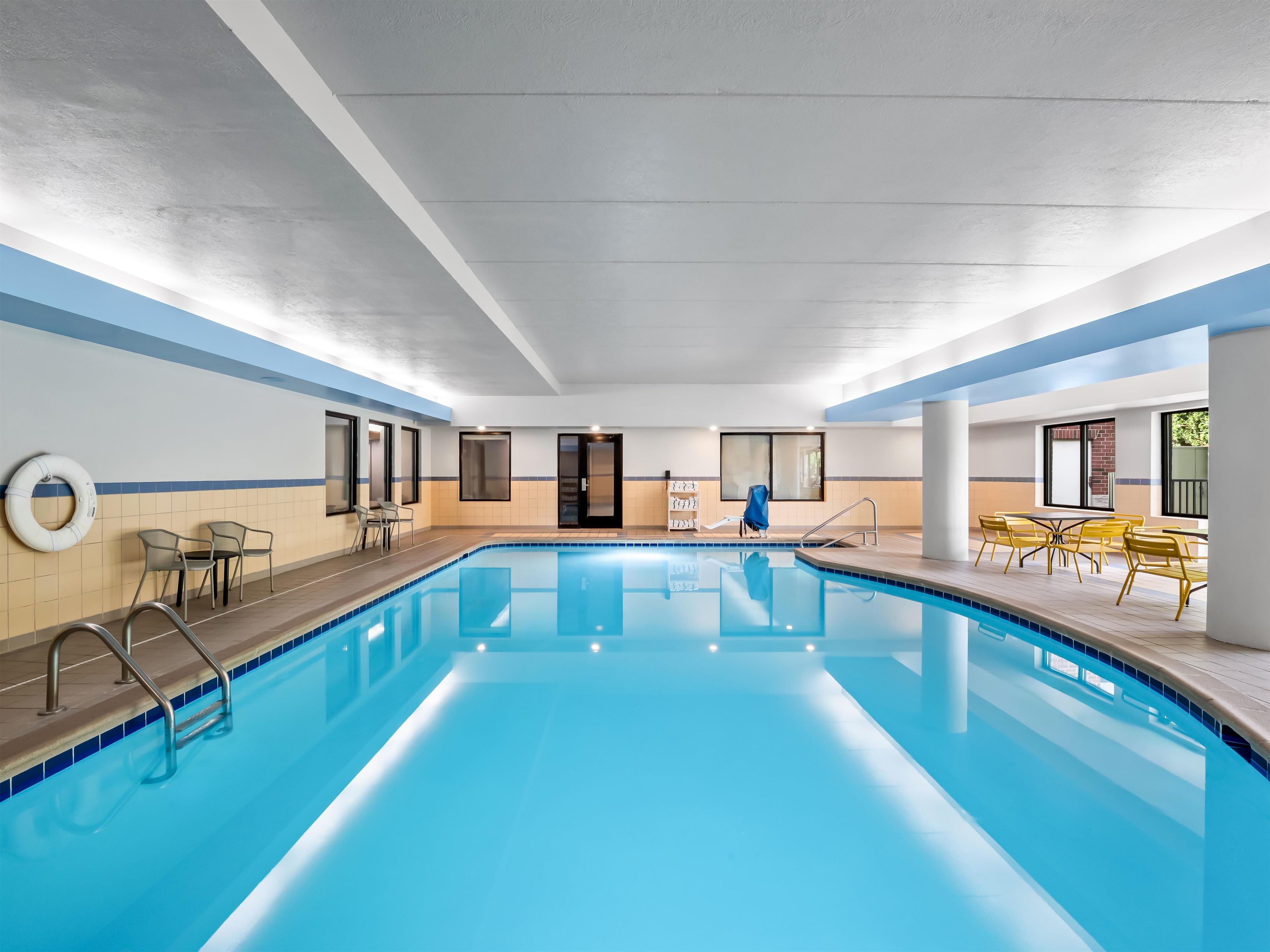 An indoor swimming pool with clear water, surrounded by seating areas and a lifebuoy on the wall.