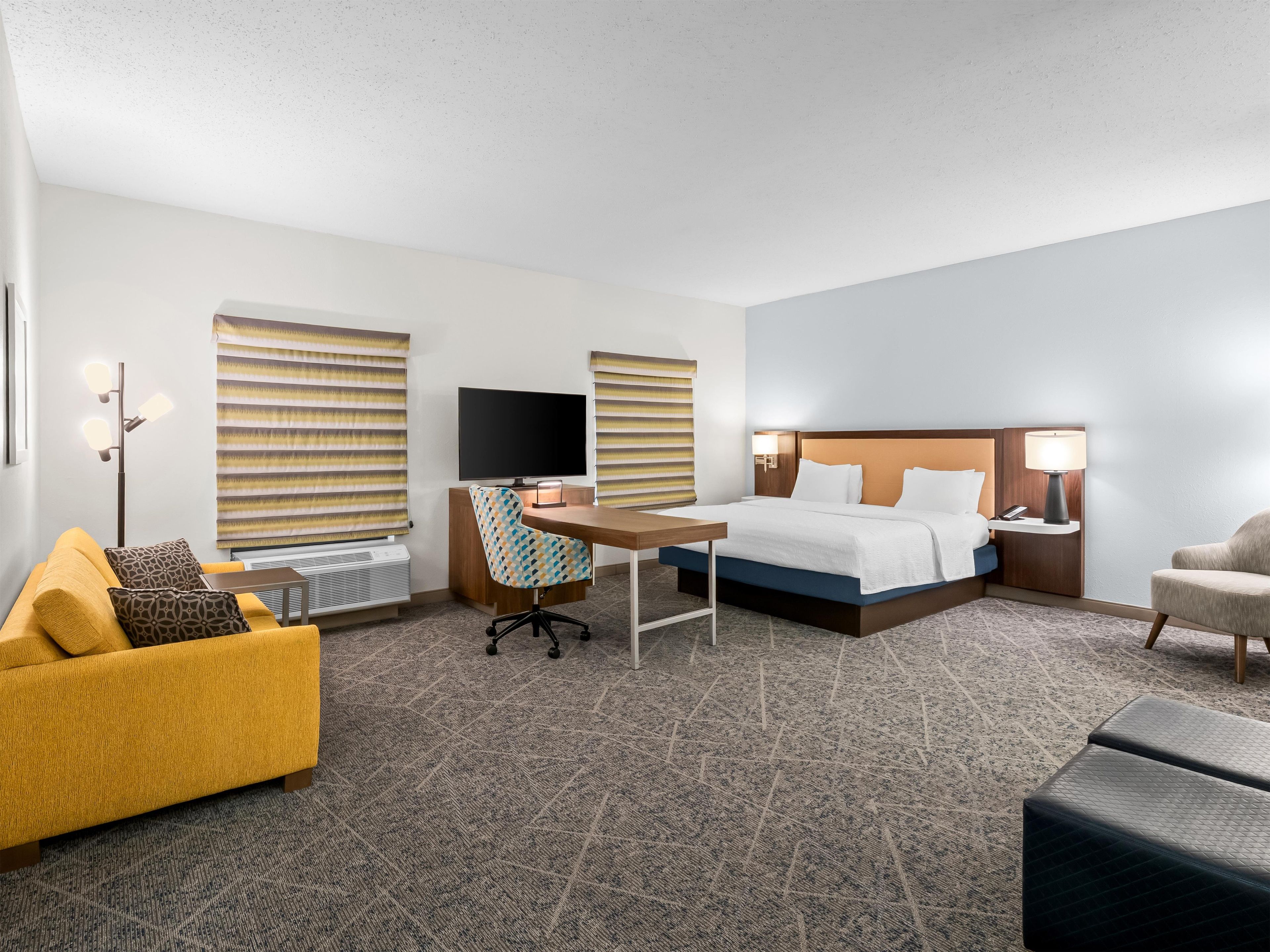 Habitación de hotel con cama, escritorio, silla, sofá, televisión y lámpara.