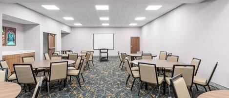 A conference room with multiple tables and chairs, a projector screen, and a carpeted floor.
