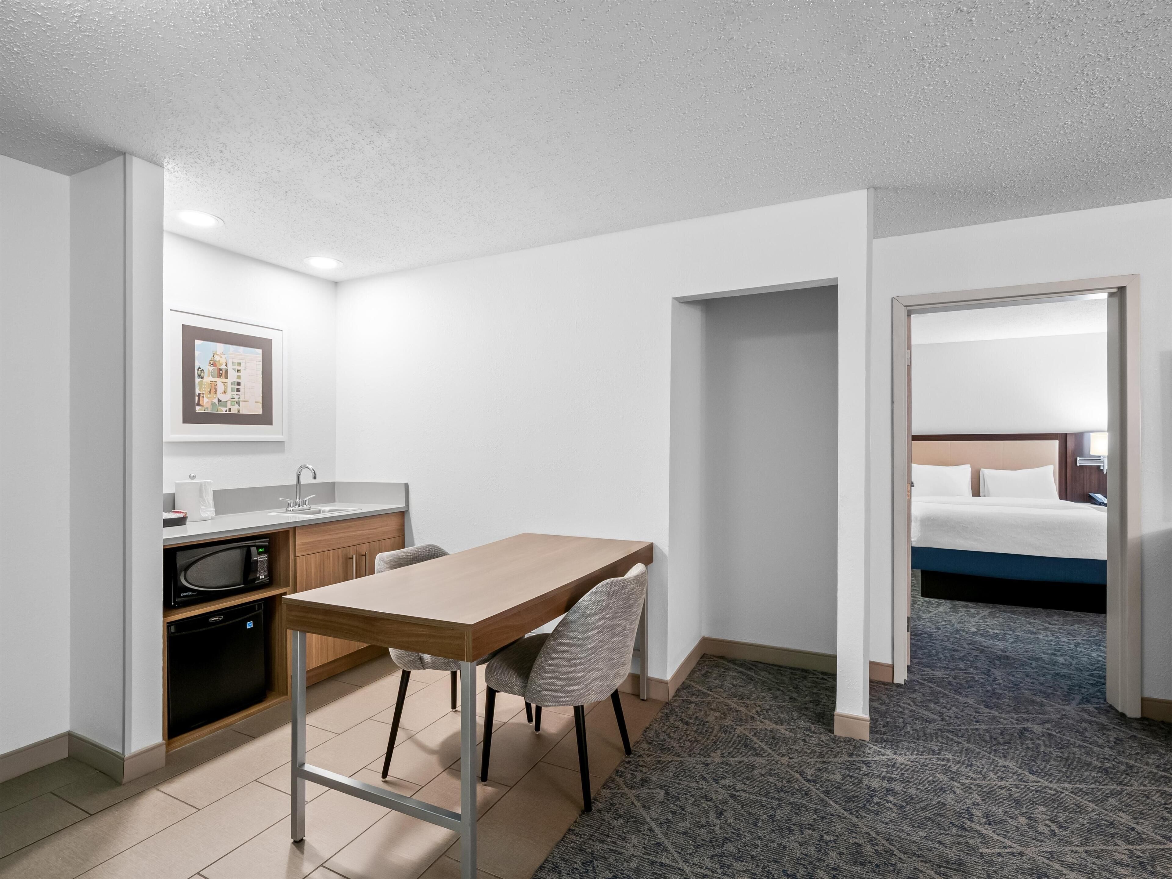 A hotel room with a kitchenette, a dining area, and a bed.
