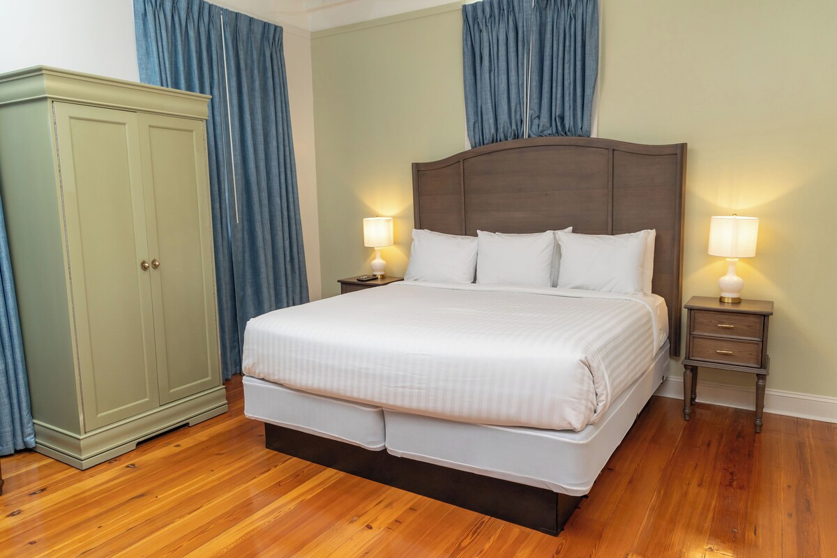 A neatly made bed with white bedding, two bedside tables with lamps, a wardrobe, and wooden flooring.